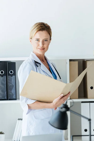 Adulto Feminino Médico Casaco Branco Segurando Pasta Olhando Para Câmera — Fotografia de Stock Grátis