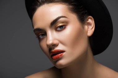 elegant model with makeup posing in stylish felt hat, isolated on grey