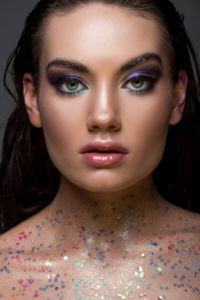 beautiful glamorous girl posing with glitter on body and looking at camera, isolated on grey