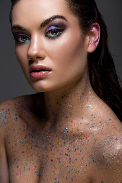 attractive glamorous young woman posing with glitter on naked body for fashion shoot, isolated on grey