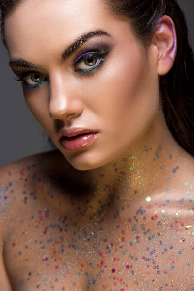 stylish young woman posing with glitter on body for fashion shoot, isolated on grey