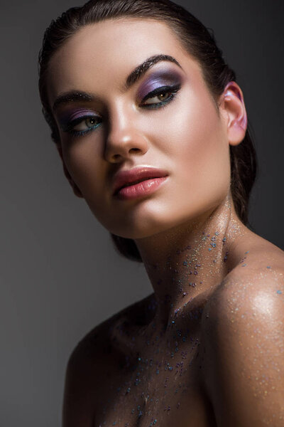 glamorous girl posing with glitter on body for fashion shoot, isolated on grey