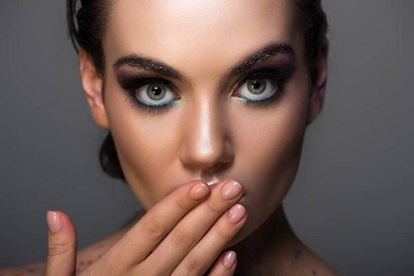 young woman with makeup gesturing oops sign, isolated on grey