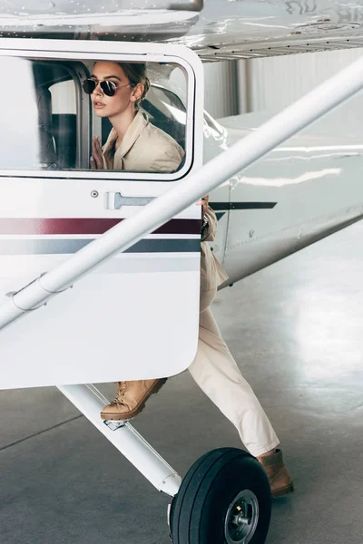 时尚的年轻女子在太阳镜和夹克登机在飞机上 — 免费的图库照片