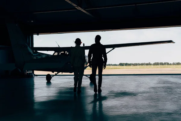 Tampilan Belakang Siluet Pasangan Stylish Berjalan Dekat Pesawat Hangar — Stok Foto