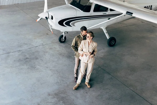 High Angle View Young Couple Stylish Jackets Embracing Hangar Airplane — Free Stock Photo