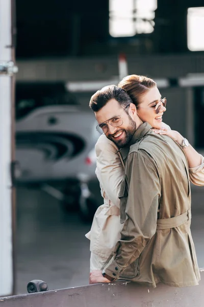 Happy Man Eyeglasses Jacket Looking Camera While Embracing Girlfriend Hangar — Stock Photo, Image