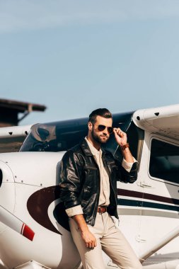 kendine güvenen erkek pilot deri ceket ve uçak poz güneş gözlüğü