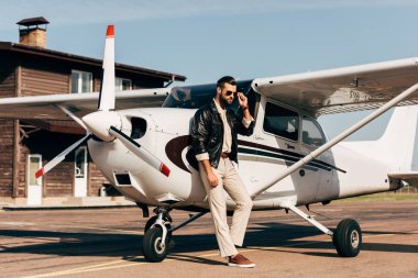 Genç erkek pilot deri ceket ve uçak poz güneş gözlüğü