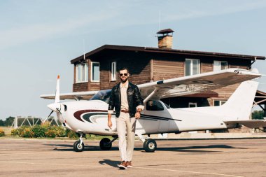 şık genç erkek pilot deri ceket ve uçak yürüyüş güneş gözlüğü