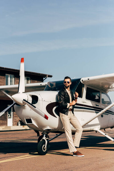 stylish man in leather jacket and sunglasses standing near airplane 