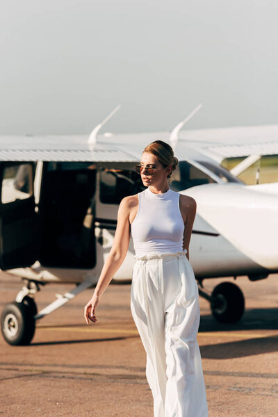 stylish beautiful young woman in sunglasses walking near airplane