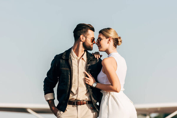 side view of young stylish couple in sunglasses standing face to face 