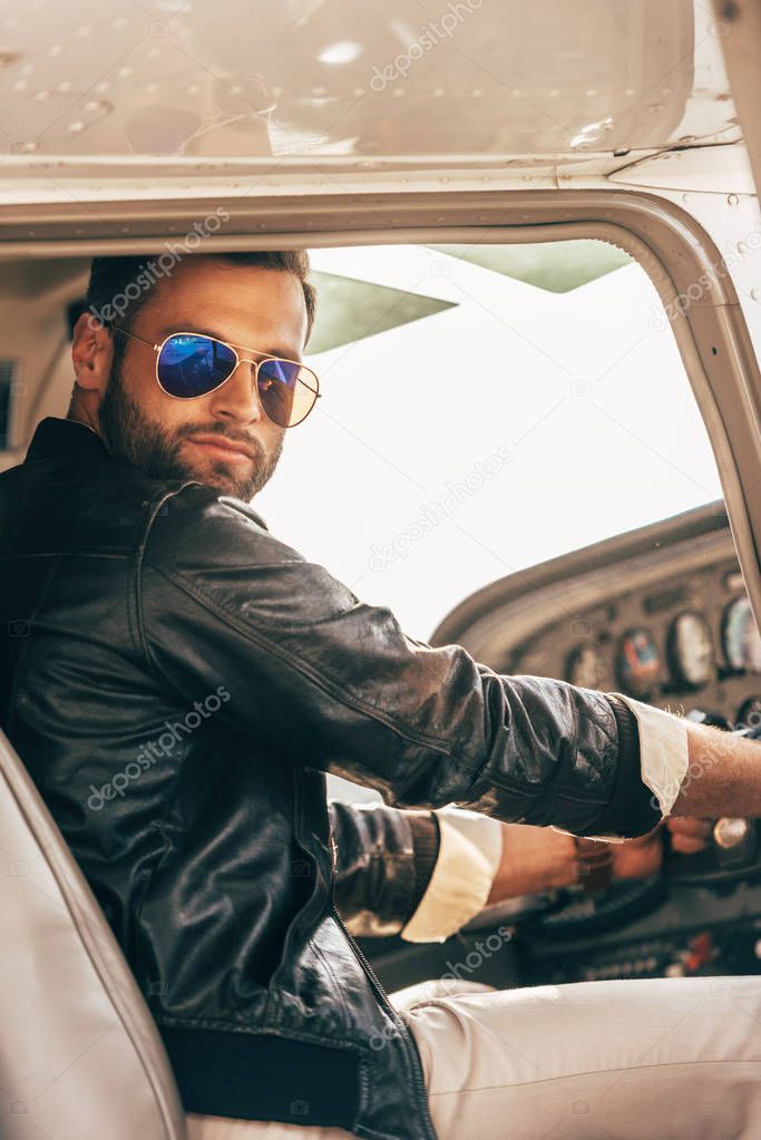 stylish male pilot in leather jacket and sunglasses sitting in airplane 