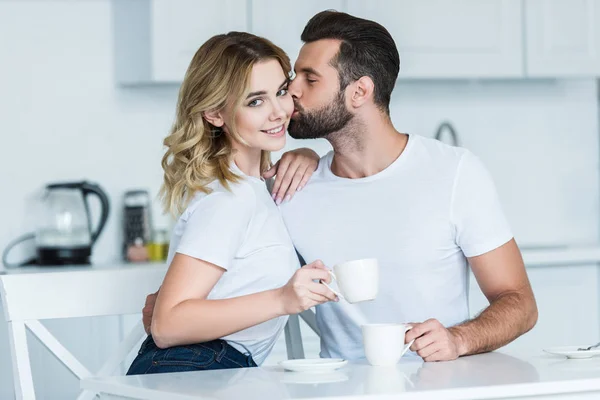 英俊的年轻人亲吻美丽的女朋友微笑在照相机 当一起喝咖啡时 — 图库照片