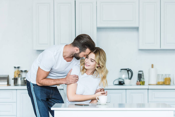 happy young couple embracing during breakfast in kitchen