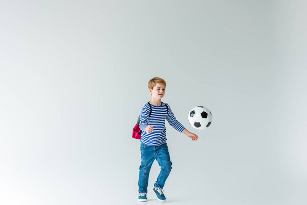 очаровательный школьник с рюкзаком играть в футбол на белом
