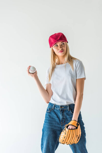 attractive baseball player in red cap holding baseball ball and looking away isolated on white