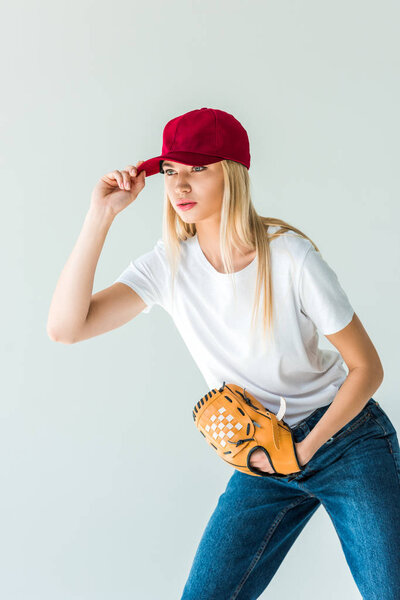 attractive baseball player touching red cap and holding baseball glove isolated on white