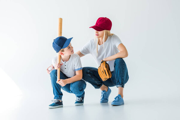 mommy and son squatting with baseball bat and glove on white and looking at each other