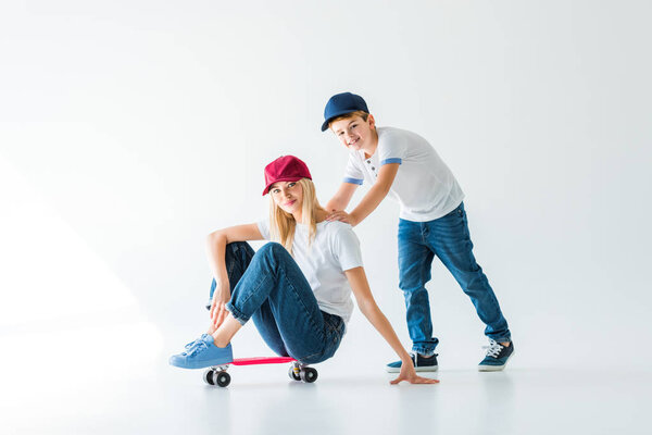 happy son pushing mother on skate on white