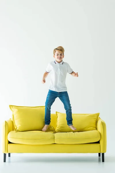 Menino Adorável Divertindo Pulando Sofá Amarelo Branco — Fotografia de Stock Grátis