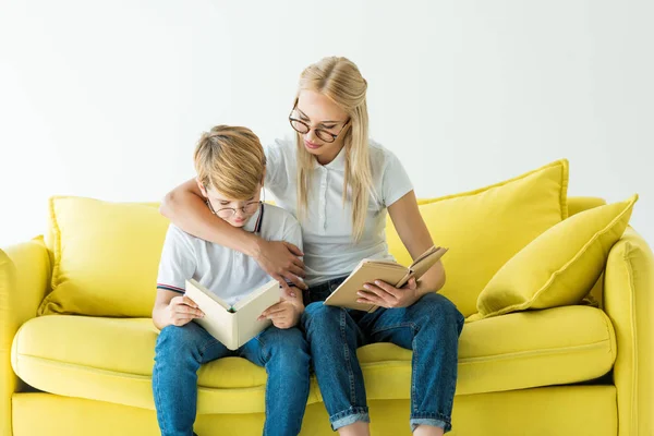 Madre Gafas Abrazando Hijo Mientras Lee Libro Sofá Amarillo Aislado — Foto de Stock