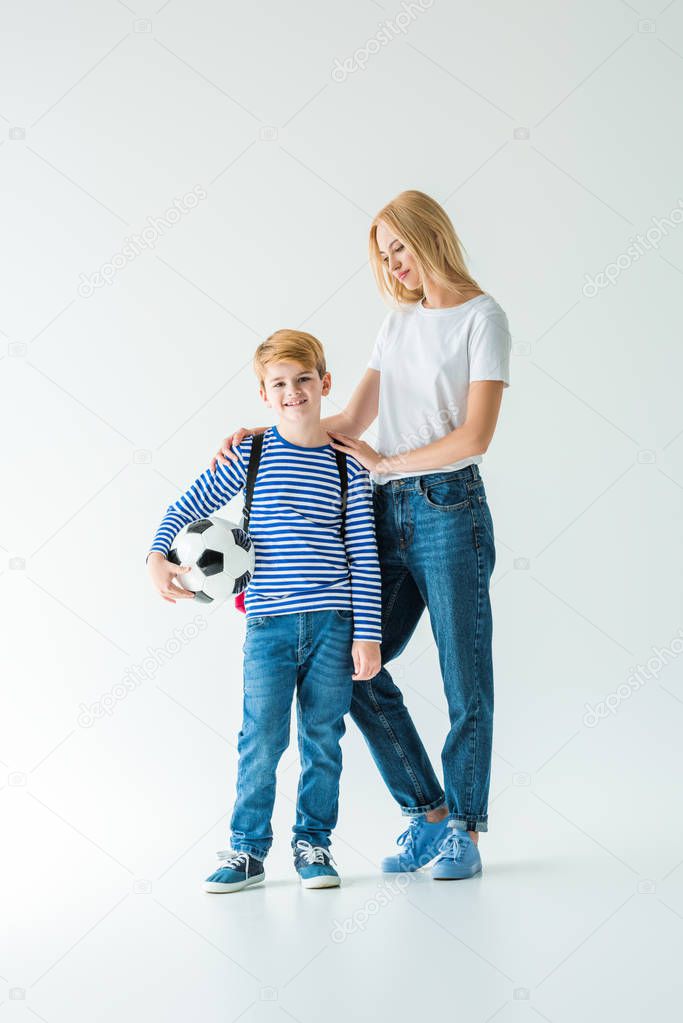 mother palming smiling son, he holding football ball on white