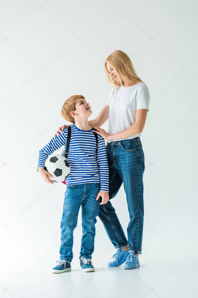 smiling mother and son looking at each other, he holding football ball on white