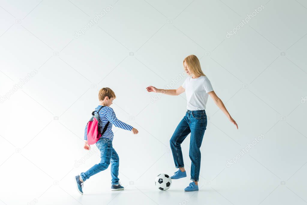 mother and son with backpack playing football on white