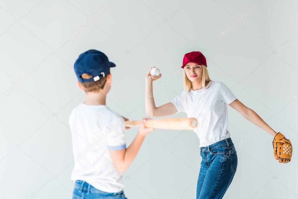 attractive mother pitching baseball ball to son with baseball bat isolated on white