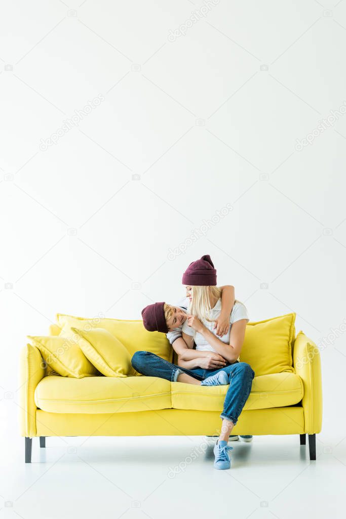 mother touching son nose on yellow sofa on white