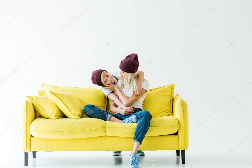 mother and son in burgundy hats hugging on yellow sofa on white