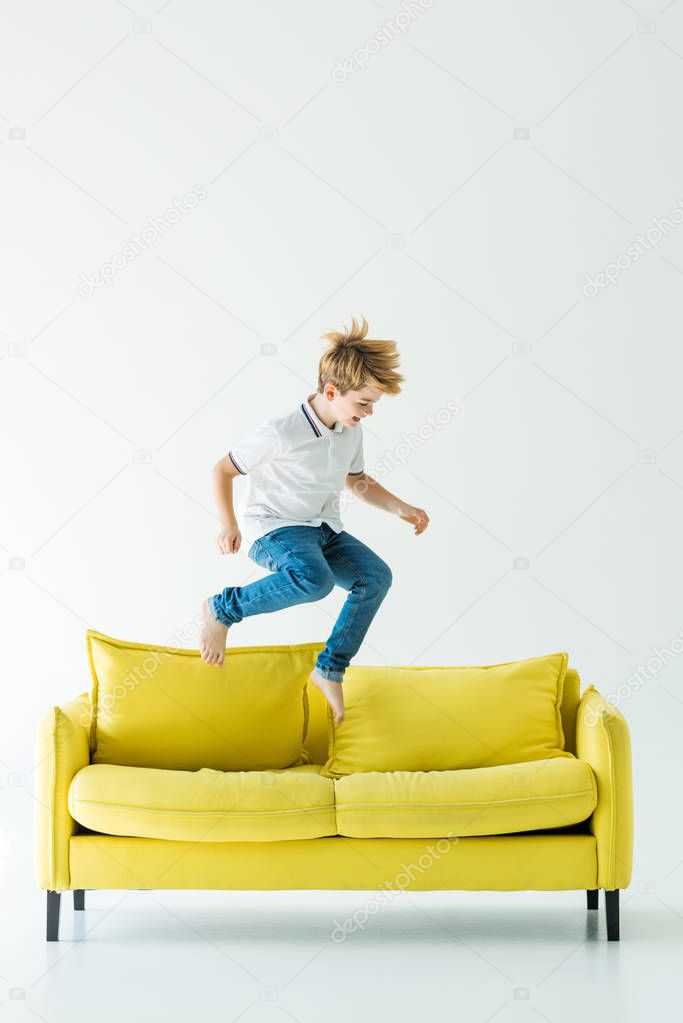 adorable boy in casual clothes jumping on yellow sofa on white