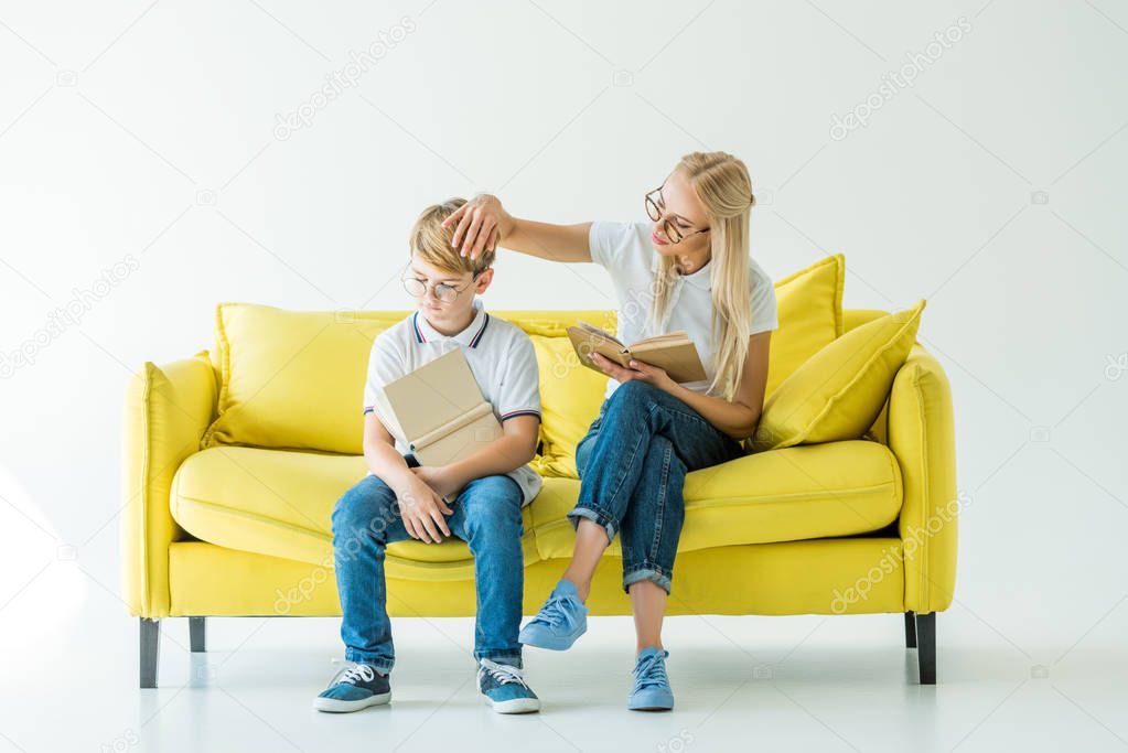 mother touching son hair while he reading book on yellow sofa