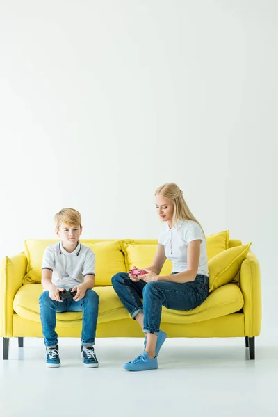 Mutter Und Sohn Sitzen Mit Gamepads Auf Gelbem Sofa Auf — kostenloses Stockfoto