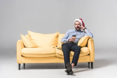 yorgun adam esniyor, kahve holding ve gri sarı koltukta oturup Noel Baba şapkası