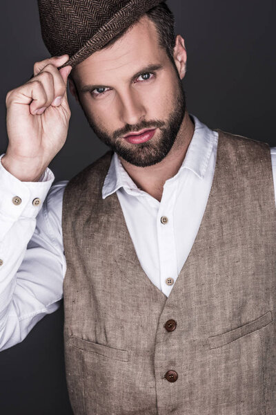 portrait of bearded man posing in hat and elegant vest, isolated on grey