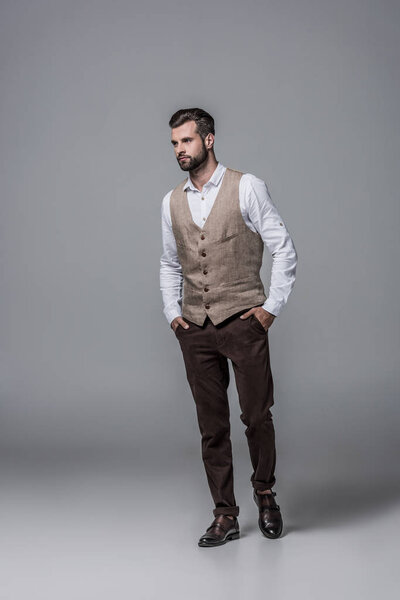 handsome bearded man posing in trendy elegant waistcoat on grey