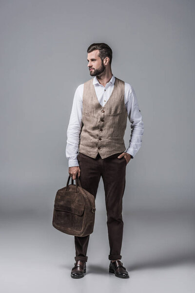 stylish elegant man in waistcoat posing with leather bag on grey