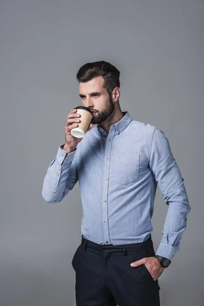 エレガントなスタイリッシュなビジネスマン グレーに分離された使い捨てのカップからコーヒーを飲む — ストック写真
