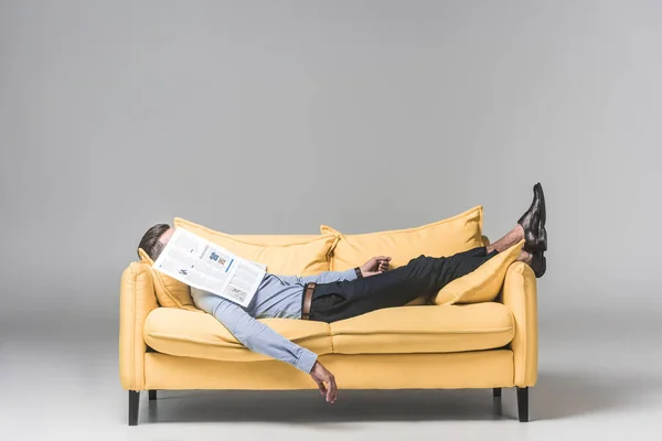 Tired businessman sleeping on yellow sofa with newspaper on face, on grey — Stock Image Tired Businessman Sleeping Yellow Sofa Newspaper Face Grey Stock Picture
