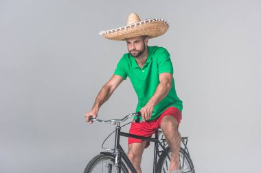 handsome man in mexican sombrero riding bike on grey clipart