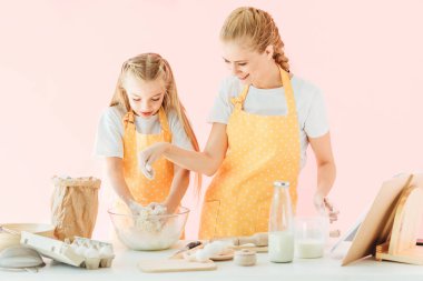 Genç Anne ve sarı önlük birlikte pink izole hamur yapma sevimli küçük kız gülümseyerek