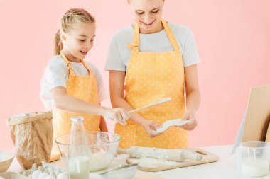 gülümseyen Genç Anne ve sevimli küçük kızı birlikte pink izole hamur hazırlama