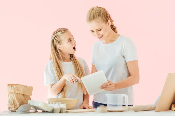 快乐的母亲和惊讶的女儿在白色 T恤使用片剂 而烹饪隔离粉红色 — 图库照片
