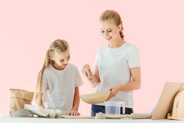 快乐的母亲和女儿在白色 T恤看着碗 而烹饪一起孤立的粉红色 — 免费的图库照片