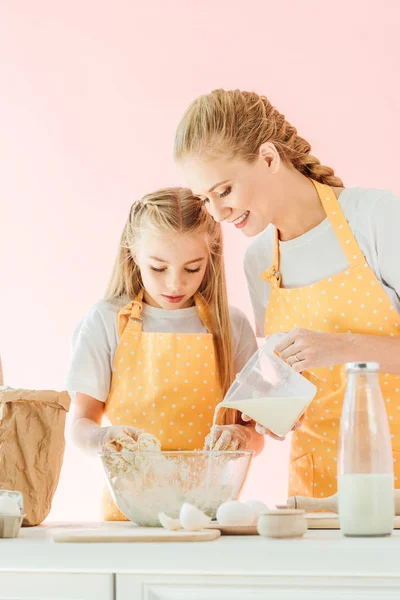 Madre Sorridente Versando Latte Pasta Mentre Figlia Impastare Isolato Rosa — Foto stock gratuita