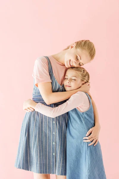 快乐的年轻母亲和女儿在蓝色的礼服拥抱在粉红色的孤立 — 图库照片
