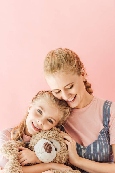 красивая счастливая мать и дочь с плюшевым мишкой изолированы на розовый
